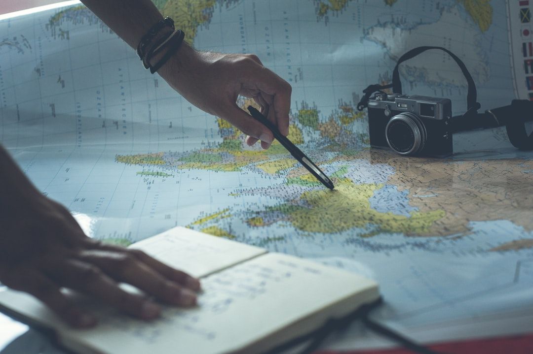 Main qui trace un itinéraire sur une carte, carnet ouvert et appareil photo