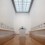 Galerie d'art contemporain avec œuvres exposées sous éclairage professionnel et visiteurs admirant les toiles